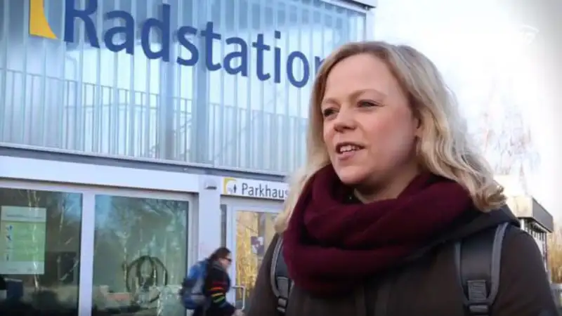 Maraike Kahlstorf von Rewe steht vor einem Gebäude mit der Aufschrift "Radstation". Sie trägt einen roten Wollschal