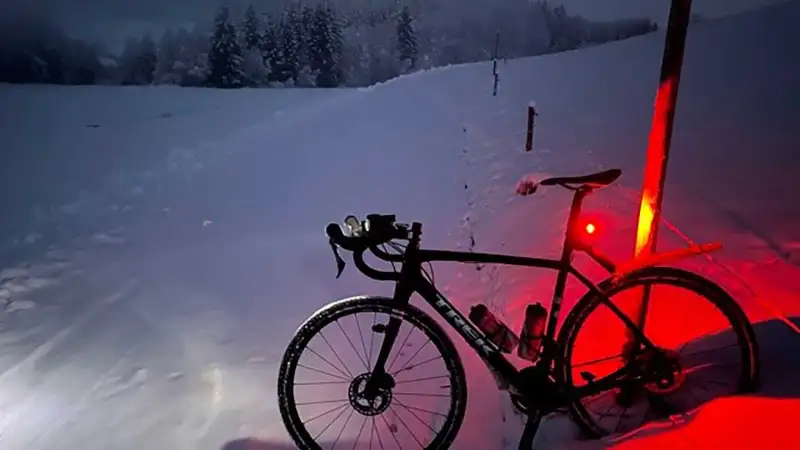 Ein Mountainbike auf verschneitem Feldweg, in der Dämmerung leuchtet das Rücklicht rot auf dem Schnee