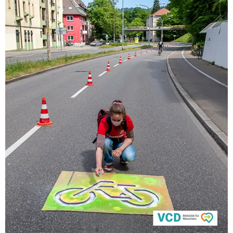 Vertreterin des Verkehrsclub Deutschland sprüht Fahrrad auf Straße in Freiburg