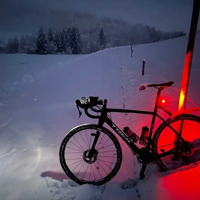 Ein Mountainbike auf verschneitem Feldweg, in der Dämmerung leuchtet das Rücklicht rot auf dem Schnee