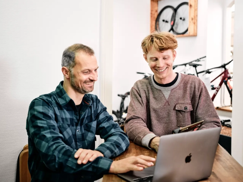 Zwei Männer im Fachhandel am Laptop an der Theke im Hintergrund Fahrräder