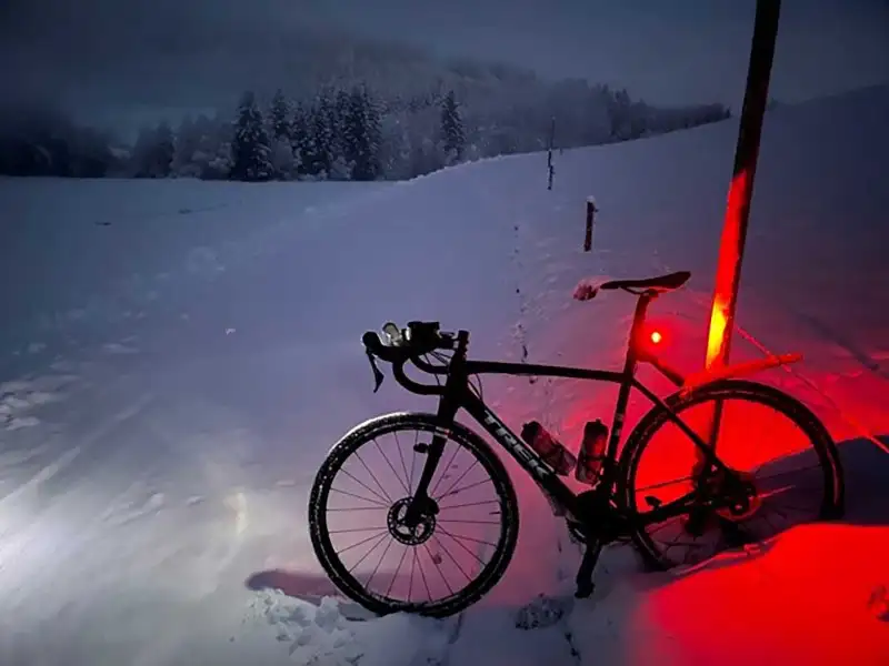 Ein Mountainbike auf verschneitem Feldweg, in der Dämmerung leuchtet das Rücklicht rot auf dem Schnee