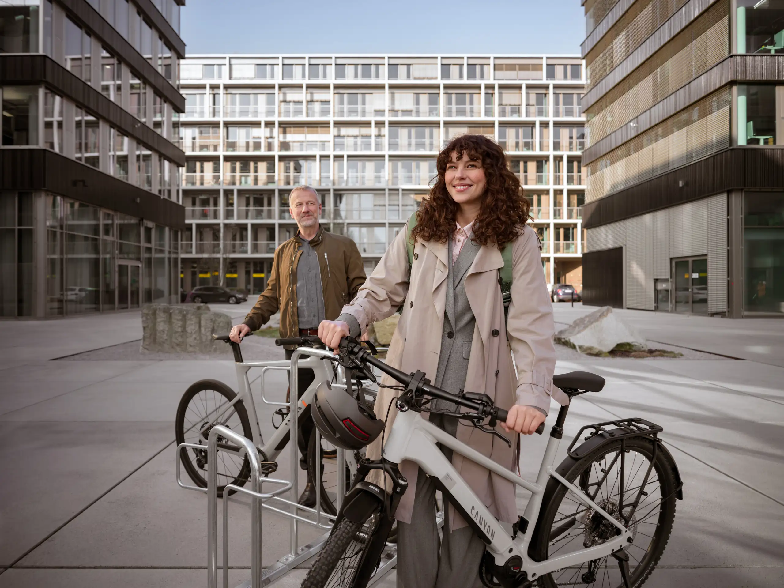 JobRadlerin steht mit Fahrrad abfahrbereit auf einem Firmencampus, im Hintergrund Kollege mit Fahrrad JobRadlerin steht mit Fahrrad abfahrbereit auf einem Firmencampus, im Hintergrund Kollege mit Fahrrad