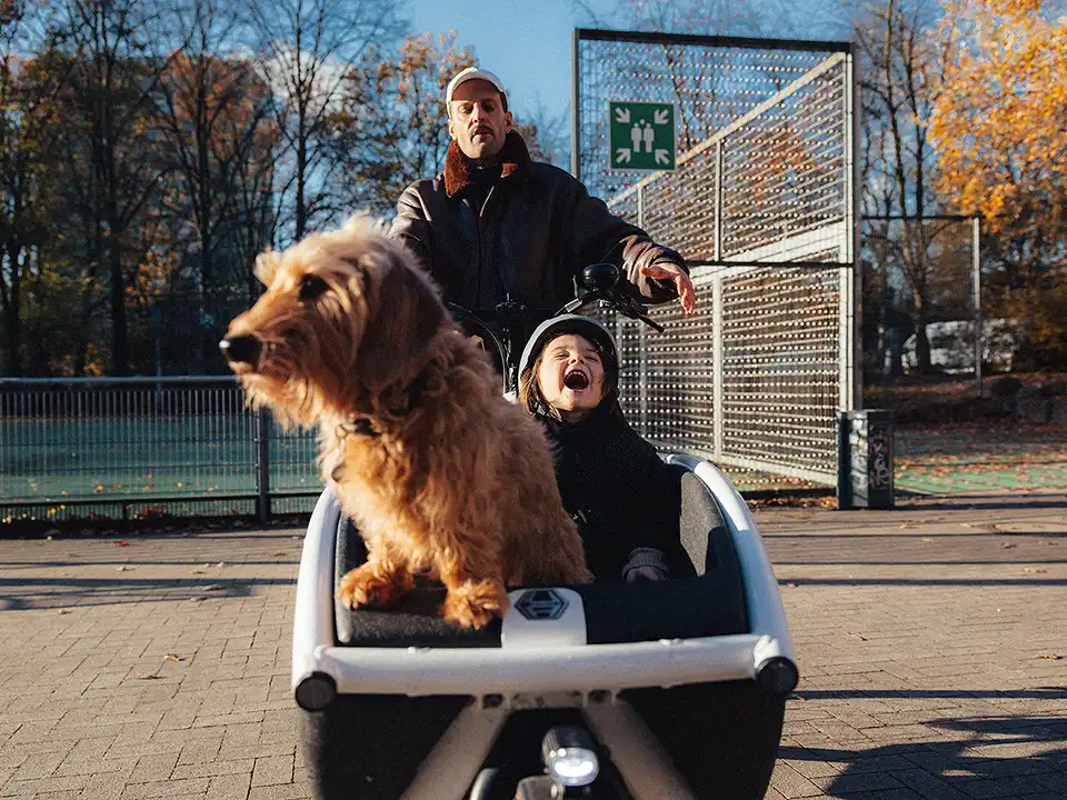 Vater mit lachender Tochter und Hund unterwegs im Lastenrad